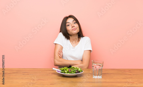 Young woman with a salad making doubts gesture while lifting the shoulders