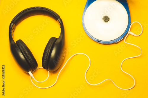Headphones with a white cable on a yellow background. compact disc player with white cd and earphones