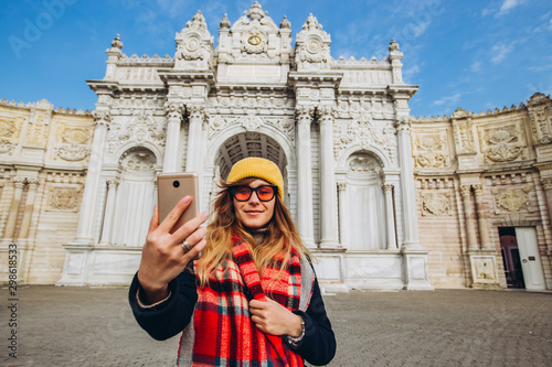 girl takes a selfie in the square in front of Dolmabahce, Istanbul, Turkey. A young girl tourist in a hat and coat is photographed on the phone in front of the Sultan's Palace in Istanbul. photo