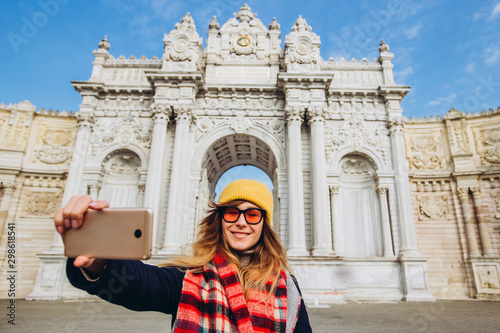 girl takes a selfie in the square in front of Dolmabahce, Istanbul, Turkey. A young girl tourist in a hat and coat is photographed on the phone in front of the Sultan's Palace in Istanbul. photo