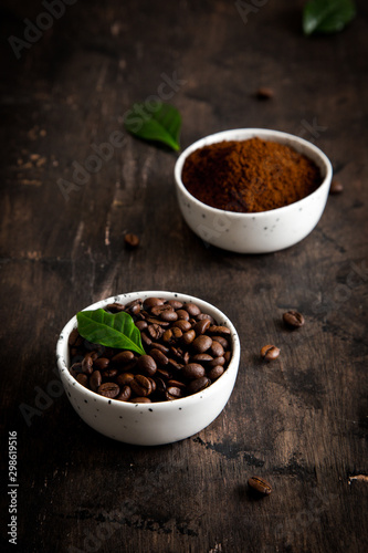 coffee beans and ground coffee in bowls with coffee tree leaf on a dark background.