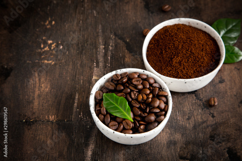 coffee beans and ground coffee in bowls with coffee tree leaf on a dark background.