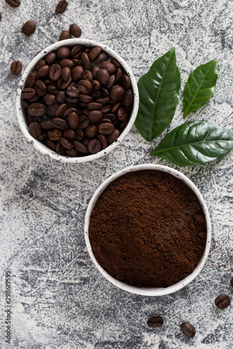 coffee beans and ground coffee in bowls with coffee tree leaf on a light background.