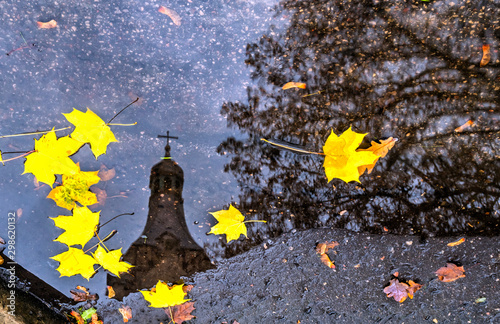 Motifs of late autumn with maple leaves and reflection of church in puddle