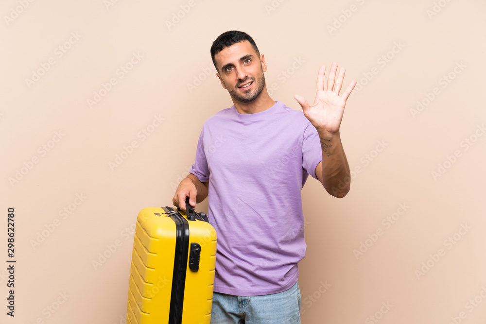 Man holding a suitcase over isolated background saluting with hand with happy expression Man holding a suitcase over isolated background saluting with hand with happy expression
