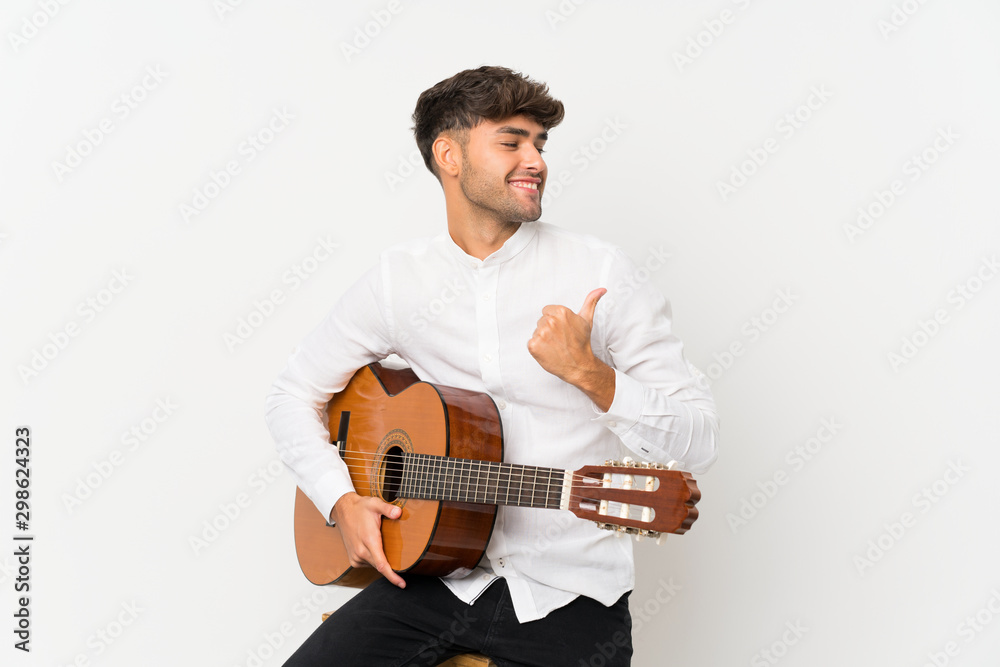 Young handsome man with guitar over isolated white background pointing to the side to present a product