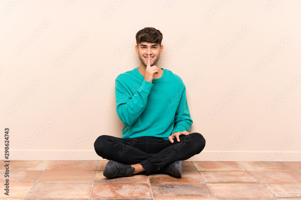 Young handsome man sitting on the floor doing silence gesture Young handsome man sitting on the floor doing silence gesture
