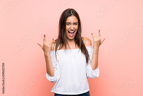 Young woman over isolated pink background making rock gesture