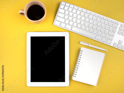 Flat lay design of modern office desk mock up with digital tablet, laptop, notebook, pen and cup of coffee on yellow background with copy space. Top view. Workspace and business concept.