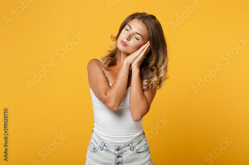 Relaxed young woman girl in light casual clothes posing isolated on yellow orange wall background studio portrait. People lifestyle concept. Mock up copy space. Sleep with folded hands under cheek.