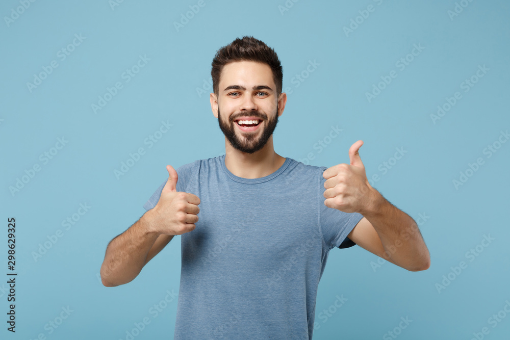 Young joyful funny smiling handsome man in casual clothes posing isolated on blue wall background, studio portrait. People sincere emotions lifestyle concept. Mock up copy space. Showing thumbs up. - obrazy, fototapety, plakaty 