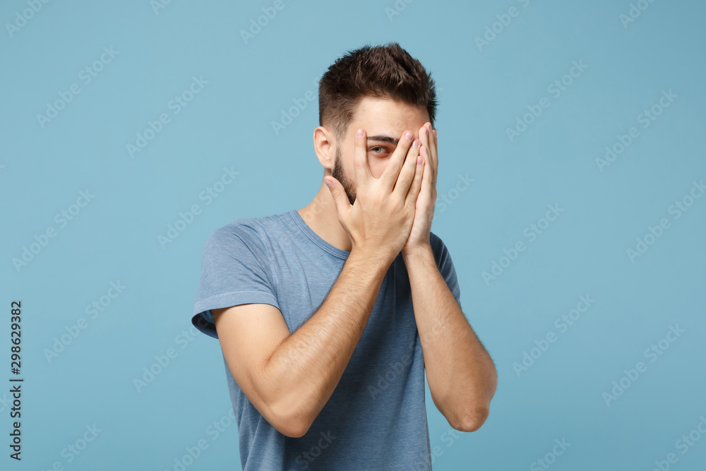 Young handsome man in casual clothes posing isolated on blue wall background, studio portrait. People sincere emotions lifestyle concept. Mock up copy space. Covering face with hands, peeping. Young handsome man in casual clothes posing isolated on blue wall background, studio portrait. People sincere emotions lifestyle concept. Mock up copy space. Covering face with hands, peeping.