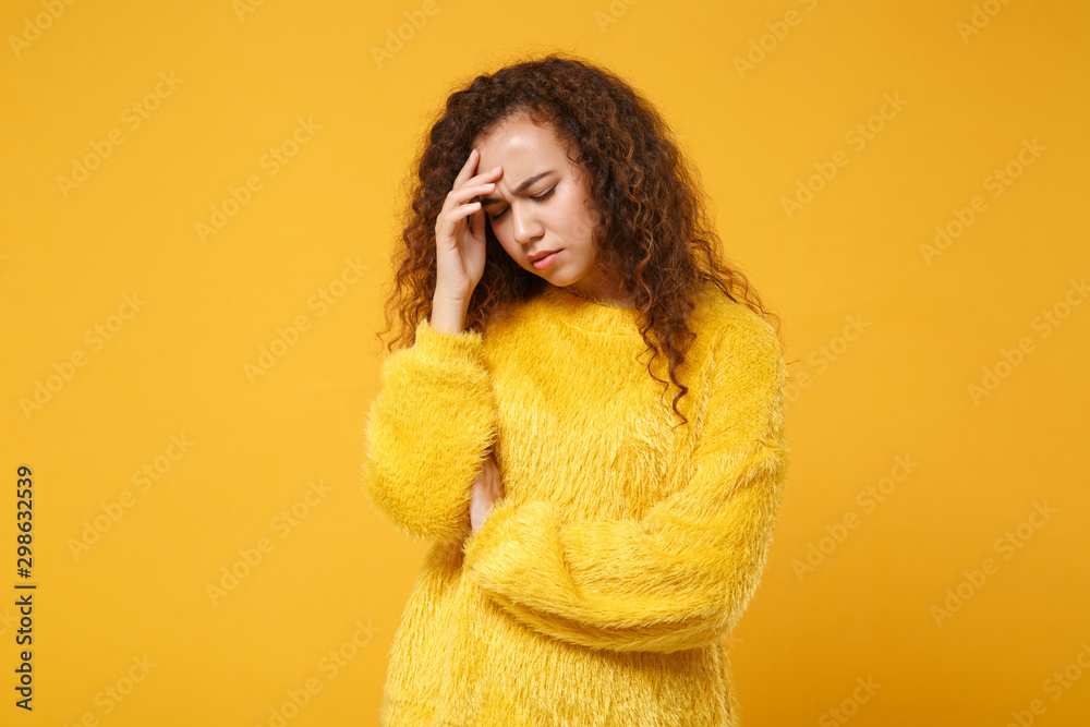 Displeased tired young african american girl in fur sweater posing isolated on yellow orange background in studio. People lifestyle concept. Mock up copy space. Keeping eyes closed, put hand on head. Displeased tired young african american girl in fur sweater posing isolated on yellow orange background in studio. People lifestyle concept. Mock up copy space. Keeping eyes closed, put hand on head.