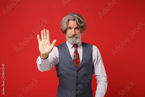Elderly gray-haired mustache bearded man in classic shirt vest colorful tie isolated on red background, studio portrait Fototapeta