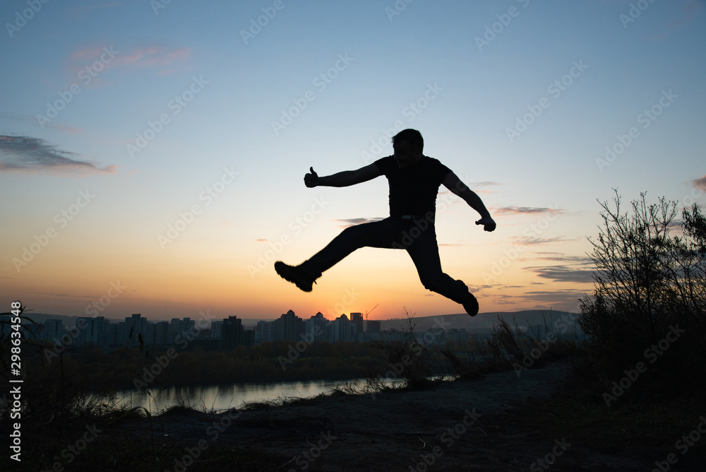 Silhouette of a jumping happy man on the background of the city and summer sunset Silhouette of a jumping happy man on the background of the city and summer sunset