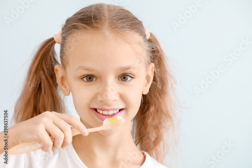 Portrait of little girl brushing teeth on light background