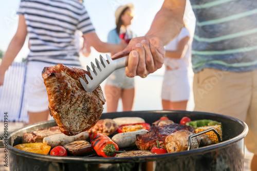 Fotografia Man cooking tasty meat on barbecue grill outdoors, closeup