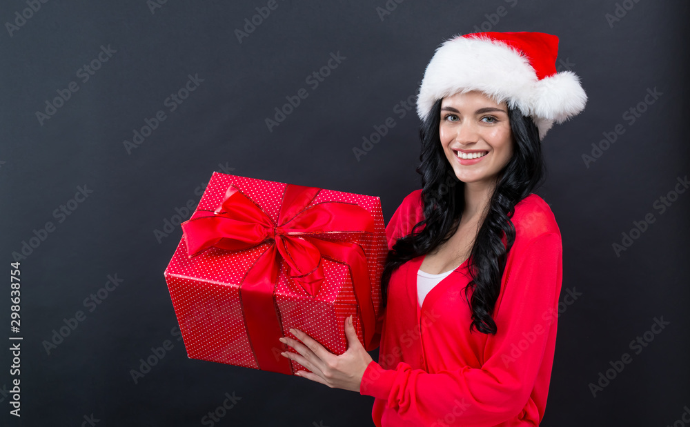 Young woman with santa hat holding a gift box on a black background Young woman with santa hat holding a gift box on a black background
