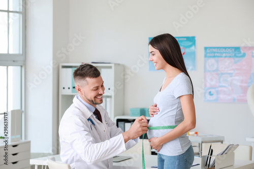 Male gynecologist taking measurements of female belly in clinic