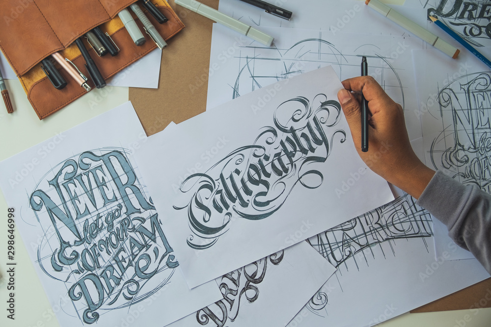 Typography Calligraphy artist designer drawing sketch writes letting spelled pen brush ink paper table artwork.Workplace design studio. Typography Calligraphy artist designer drawing sketch writes letting spelled pen brush ink paper table artwork.Workplace design studio.