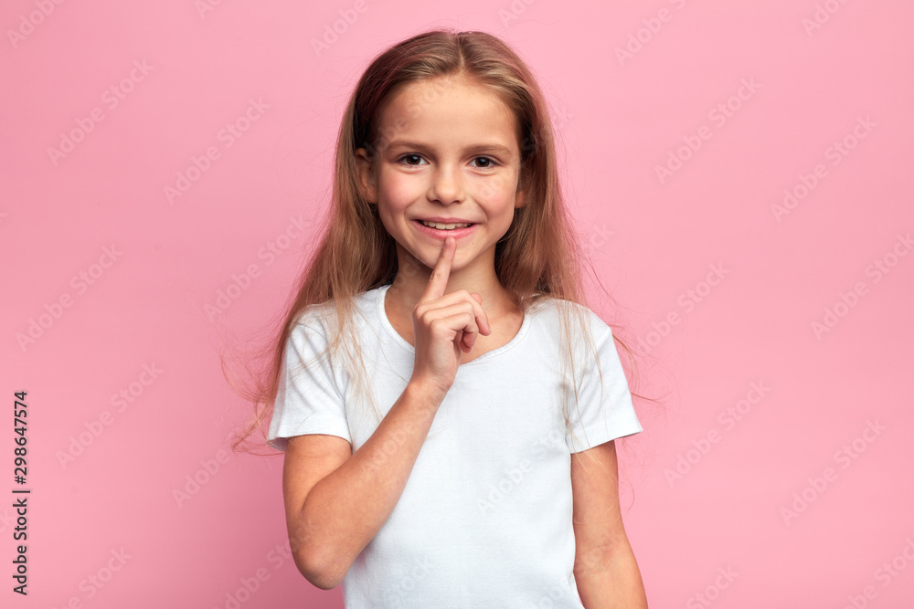 smiling cheerful adorable girl keeping her finger on her lips, asking to keep the secret. nice happy girl has a secret information. close up photo. isolated pink background smiling cheerful adorable girl keeping her finger on her lips, asking to keep the secret. nice happy girl has a secret information. close up photo. isolated pink background
