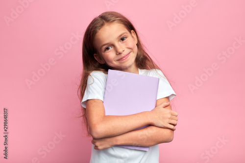 Little beautiful smiling girl holding book, going to school. close up portrait, isolated pink background, childhood. kid hugging a book. lifestyle, interest, hobby, free time, spare time