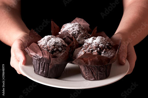 Still life with chocolate muffin with sugar. Woman hand serving or holding a white porcelain plate. Isolated on black background