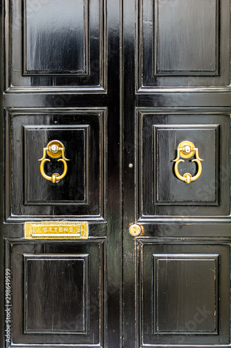 Black wooden door with golden vintage ornately shaped ring knockers and mail slot letterbox. Black door with golden hardware. © Lena Maximova