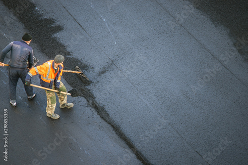 Workers lay a new asphalt coating using hot bitumen. Work of heavy machinery and paver. Top view
