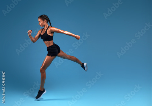 flexible strong slim sportswoman running over blue background. lifestyle, free time, spare time, copy space. isolated blue background, studio shot