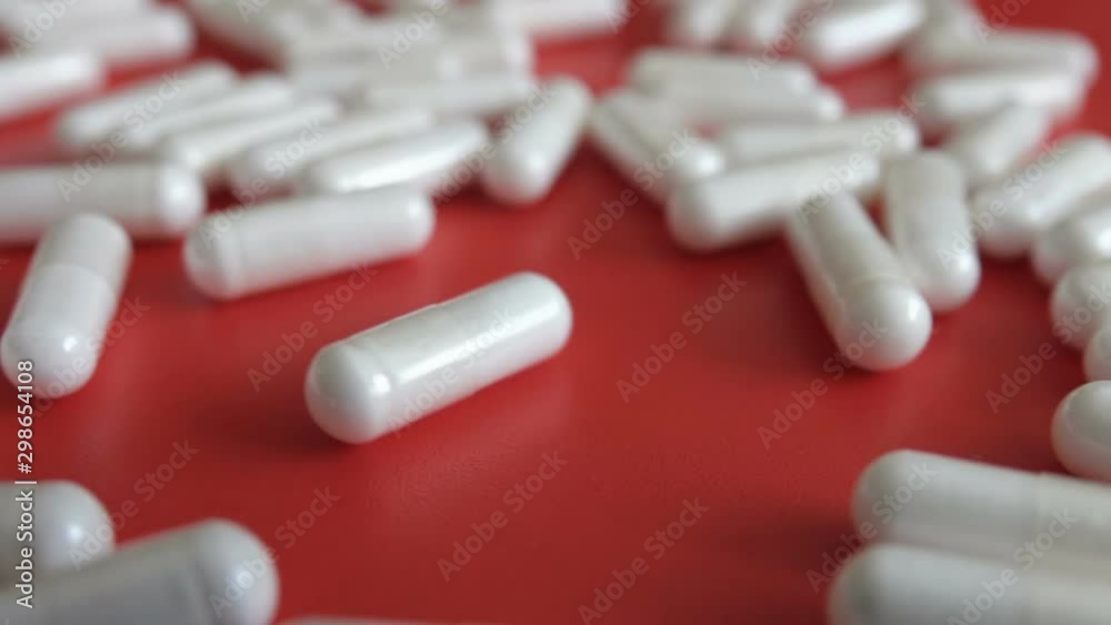 Tablets on a red background. Pills. Medicine and healthy. Close up of capsules. Many white medical capsule rotates on the red table . Slow motion. Closeup Tablets on a red background. Pills. Medicine and healthy. Close up of capsules. Many white medical capsule rotates on the red table . Slow motion. Closeup