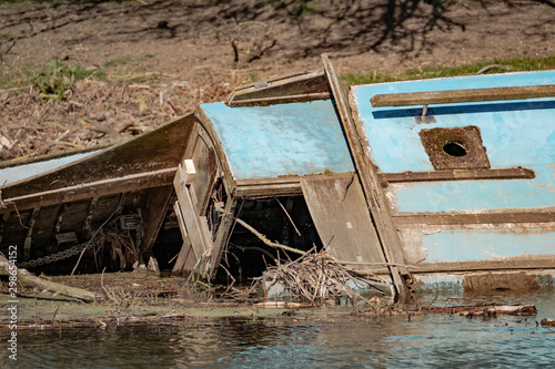 Wreck of a wooden barge seen decaying at the side of an inland waterway, showing details of the internal area, bridge and other vessel structures.