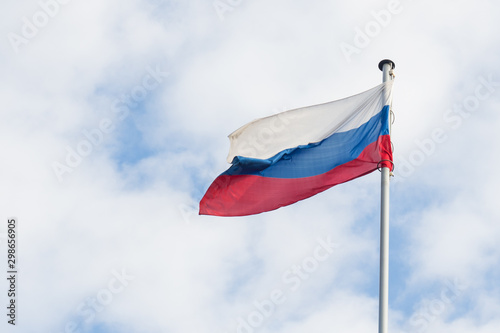 The Russian flag flies in the wind against the blue sky.