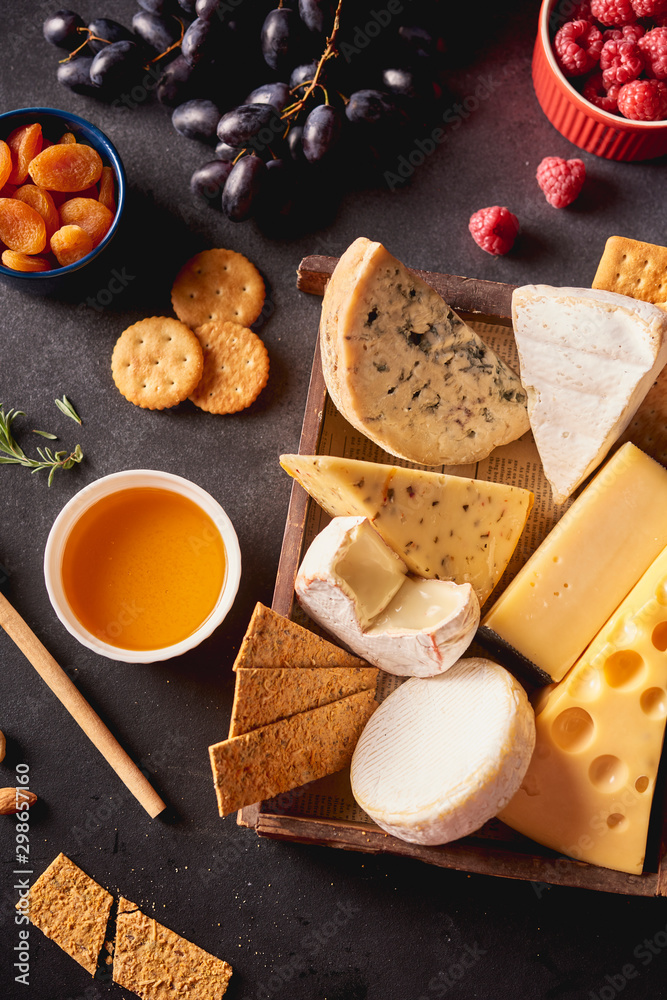 Fototapeta premium Various types of cheese in wooden box, honey, nuts, crackers, grapes