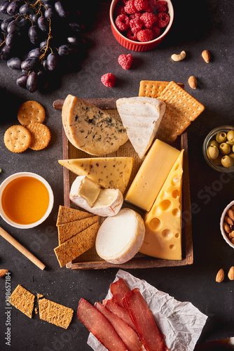 Various types of cheese in wooden box, honey, nuts, crackers, grapes