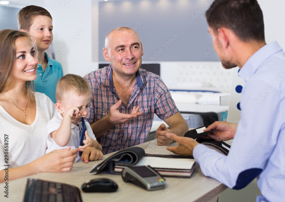 Fototapeta premium Young smiling family choosing material for mattress with salesman in salon