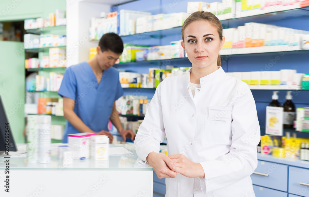 Glad pharmacist is standing near cashbox