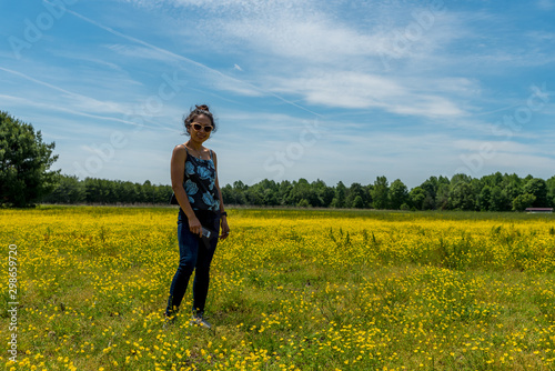 Asian woman standing in large field with yellow flowers and trees in the background