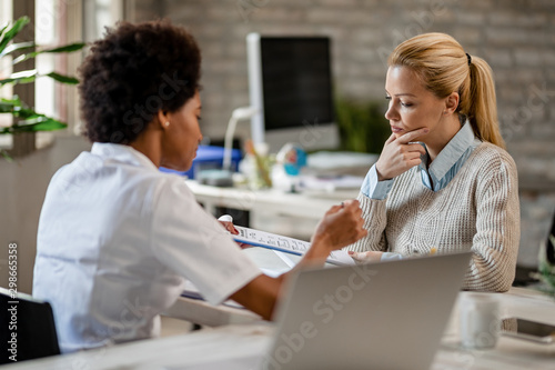 Pensive woman and her doctor analyzing medical reports at clinic.