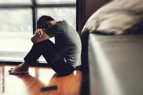 Depressed man. Sad unhappy Man sitting on the floor and holding his forehead while having headache