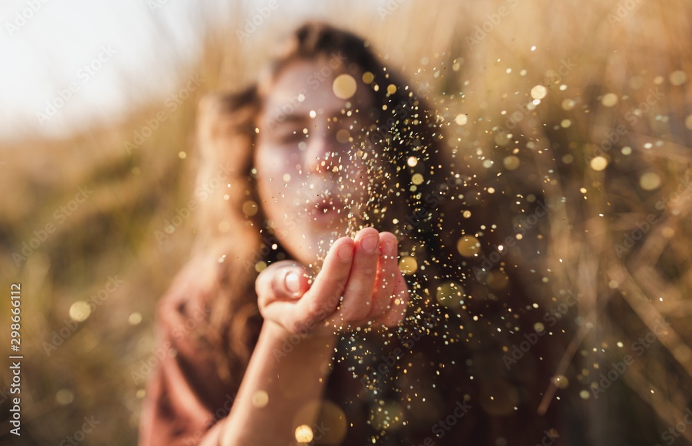 Beautiful shot of a model blowing glitter from her hand - obrazy, fototapety, plakaty 