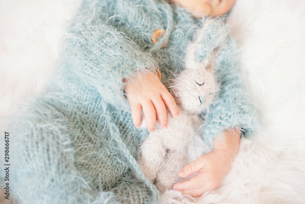 Newborn Baby. Sleeping Baby In Bed, Holding A Bunny Toy. Baby With Blue Knitted Romper Newborn Baby. Sleeping Baby In Bed, Holding A Bunny Toy. Baby With Blue Knitted Romper