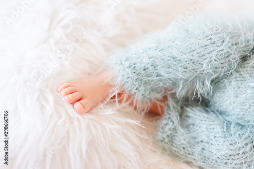 Newborn Baby Feet. Newborn Child in Blue Pants. Baby Legs In Fur Carpet