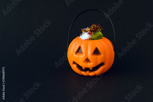 Orange plastic candy basket in the shape of a pumpkin jackolantern on a black background