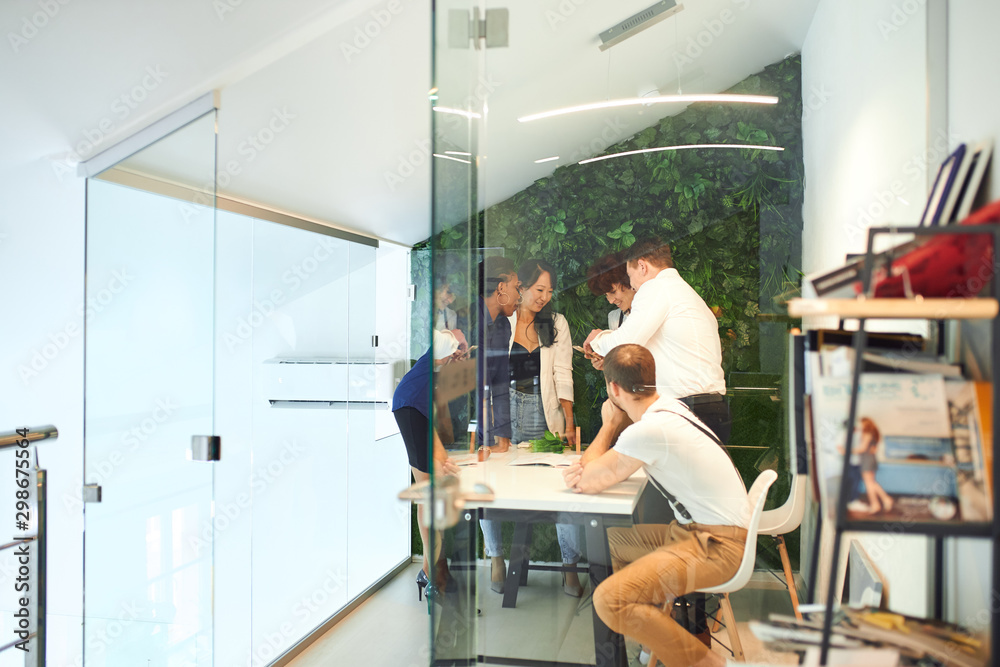 Side view on young group of business people gathered to discuss isolated in modern office with glass doors, green plants background