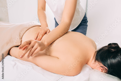 woman gets general back massage at spa center. masseur massaging back, close up