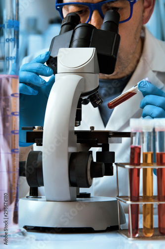 Microscopist holding a blood sample tube for analysis with the microscope in the laboratory / Laboratory technician preparing a blood sample to analyze in the lab photo