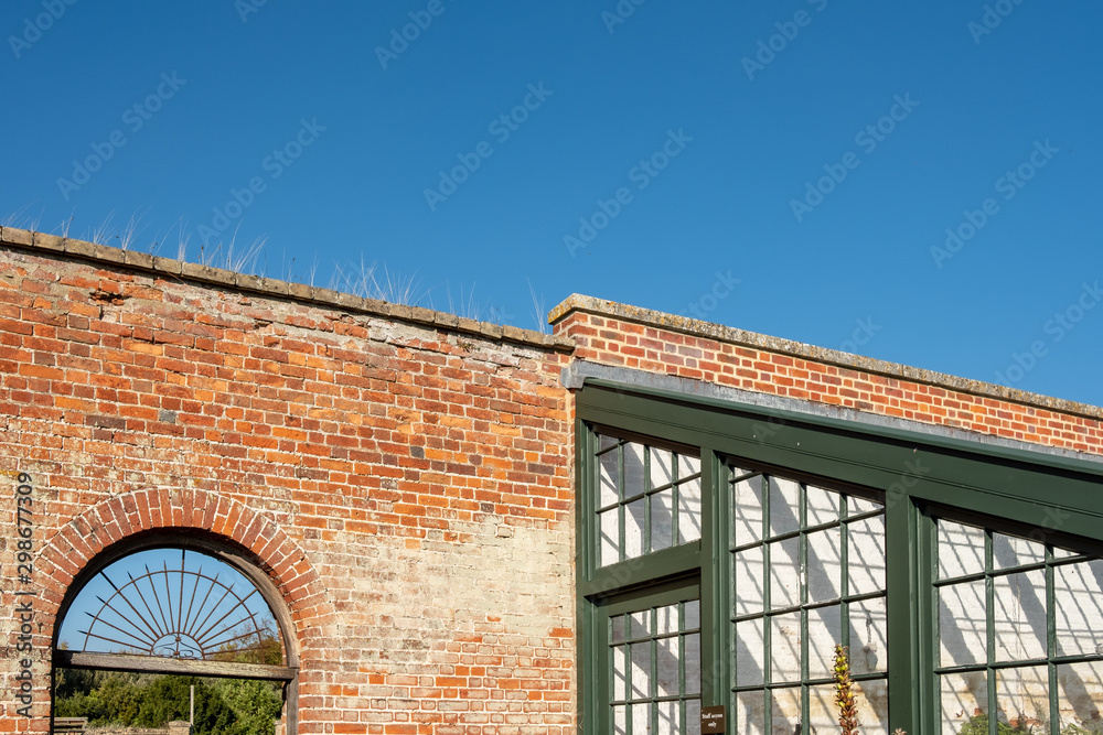 Detailed view of part of a large glass house used for plant growing. Part of a wall and entrance can be seen, leading to a walled garden.