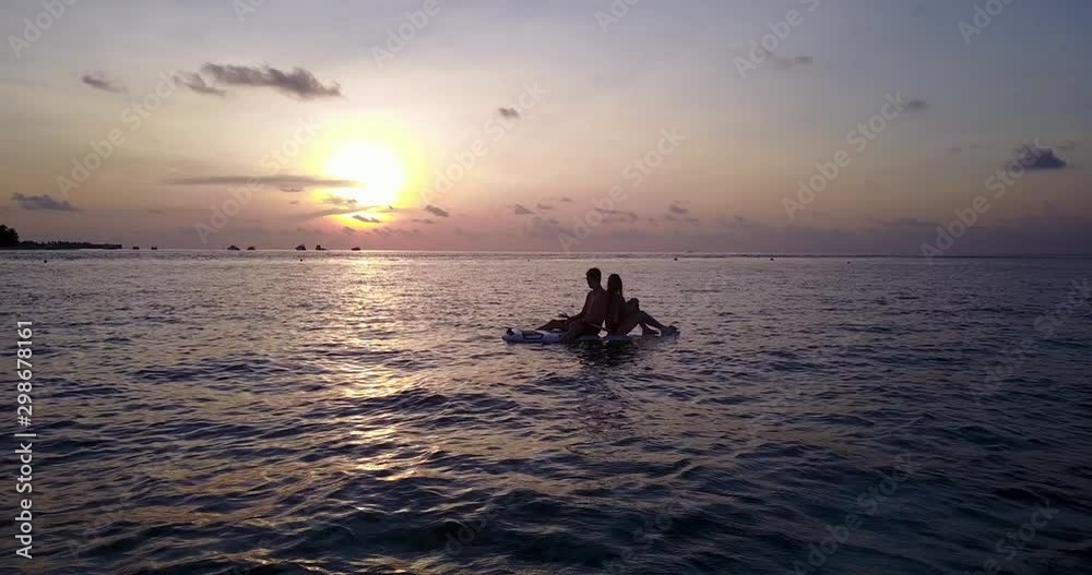 Silhouettes of young couple in love on the surfboard with beautiful red sunset as background Silhouettes of young couple in love on the surfboard with beautiful red sunset as background