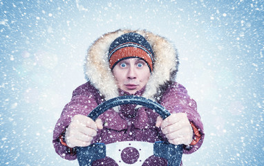 Frozen man in winter clothes drives a car in a snowstorm with his hands on the steering wheel, Front view. 